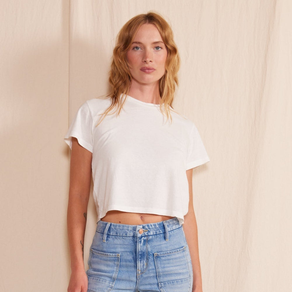 Woman wearing a white t-shirt and light blue jeans standing against a plain background