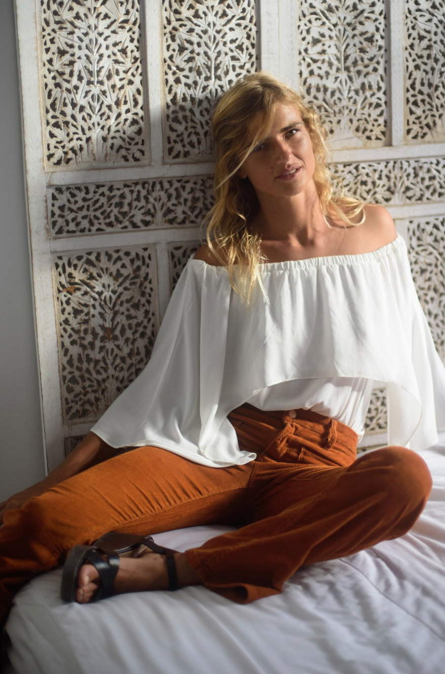 Model sitting on bed wearing the Wanderer Flare Corduroy Jeans in Whiskey - Sustainably made jeans