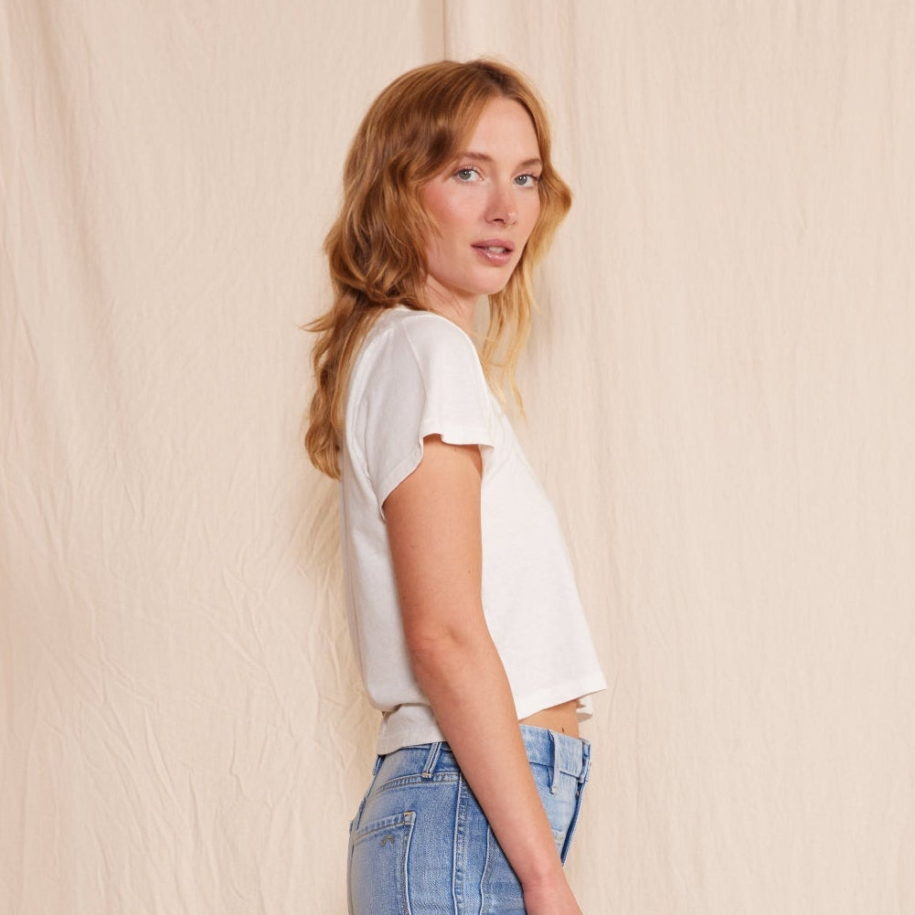 Woman wearing a white t-shirt and light blue flared jeans standing against a plain background