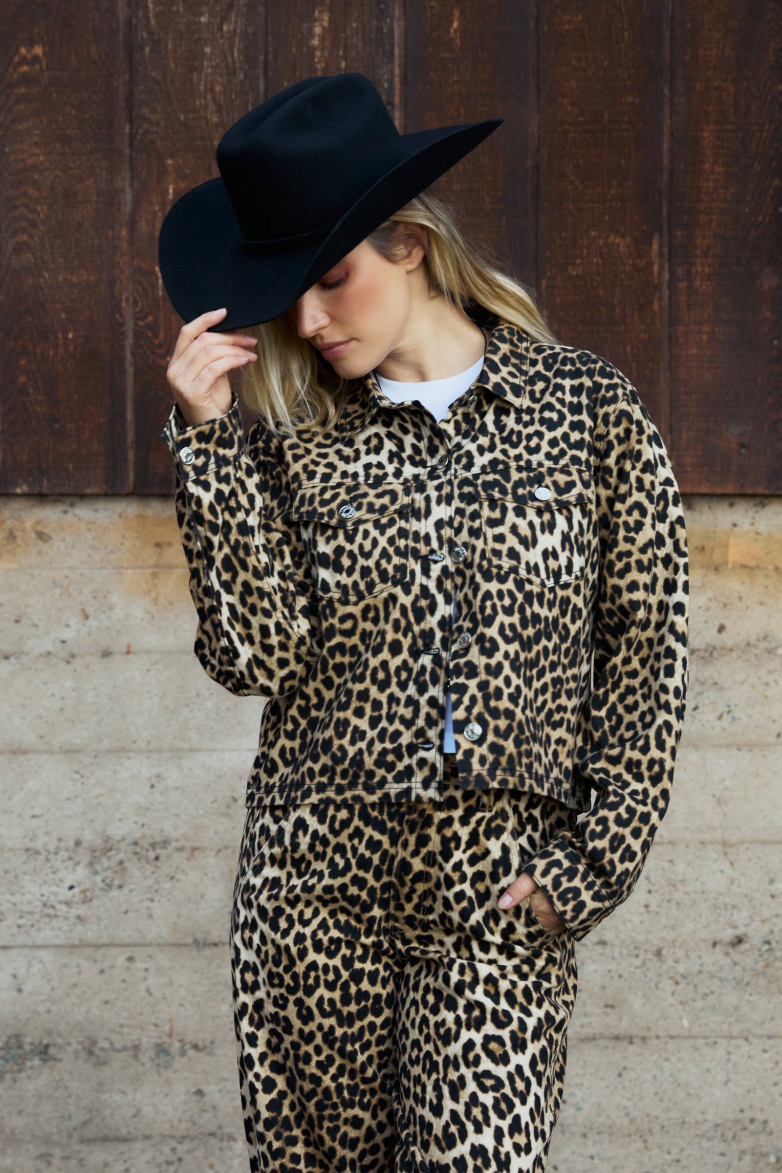 Person wearing a leopard print outfit with a black hat against a wooden background