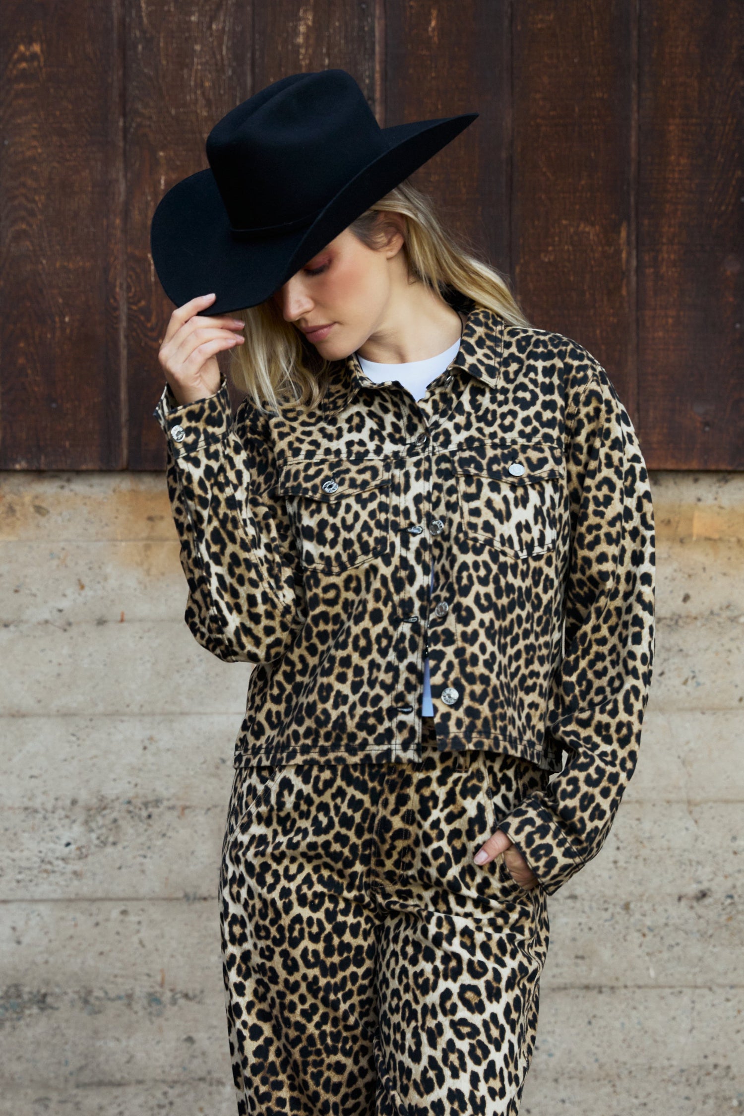 Person wearing a leopard print outfit with a black hat against a wooden background