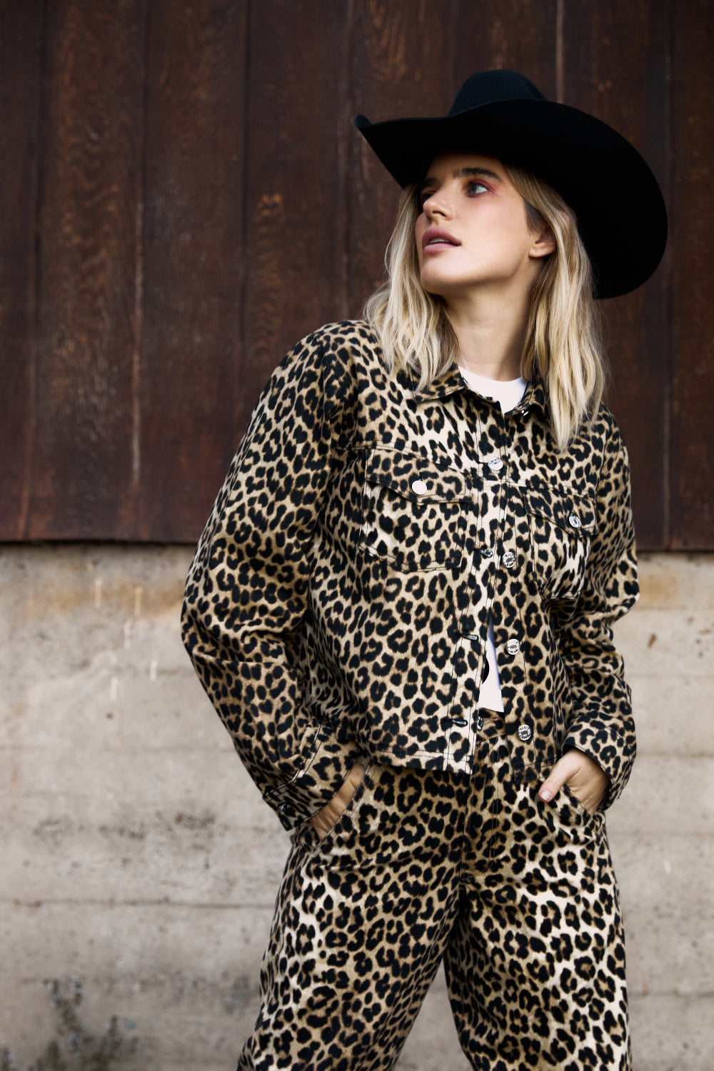 Person wearing a leopard print outfit and black hat against a wooden background