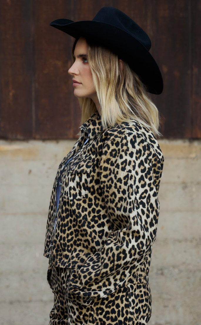 Woman wearing a leopard print jacket and black hat against a wooden background