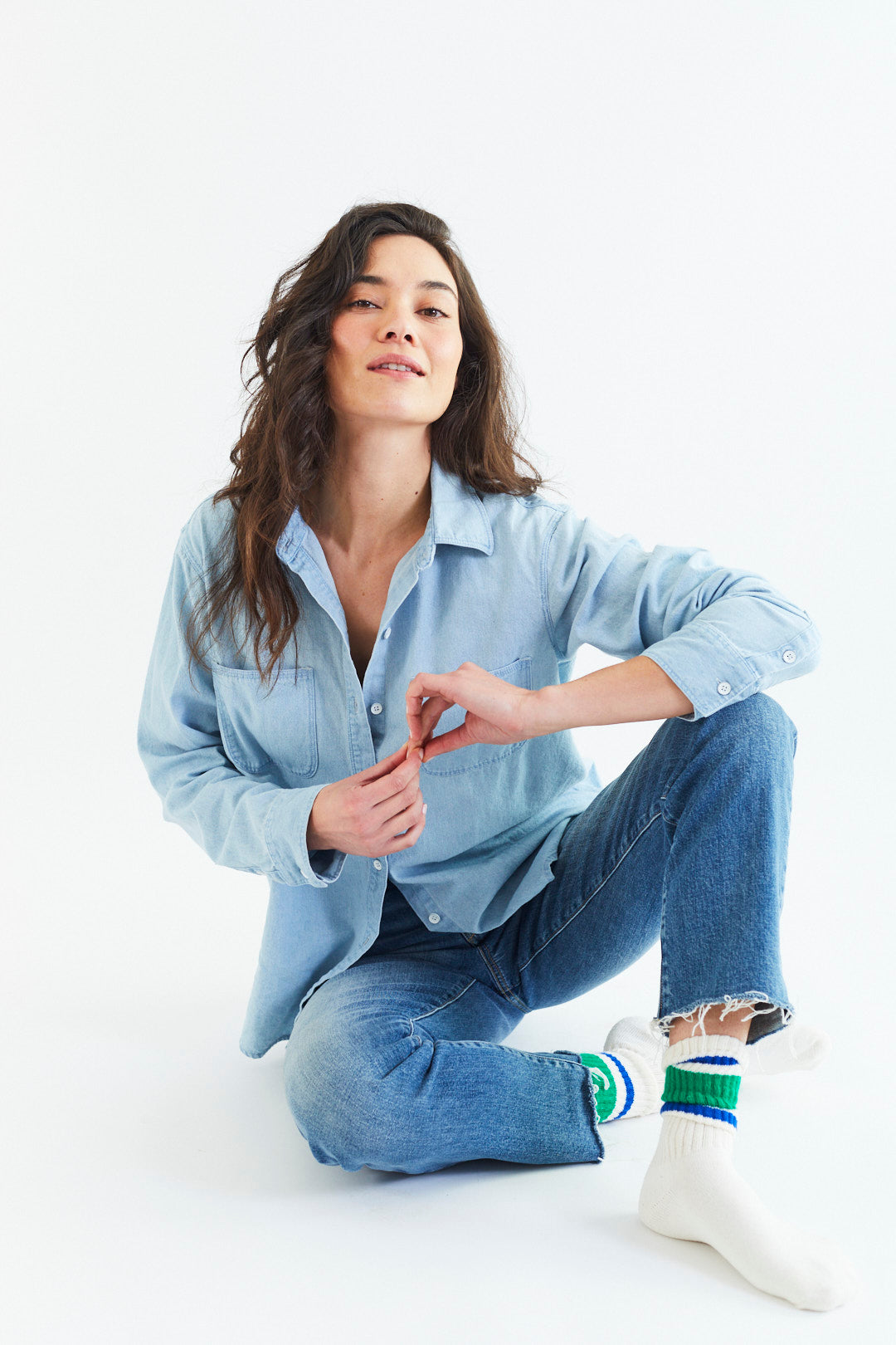 Woman wearing a light blue shirt and jeans sitting on a white background
