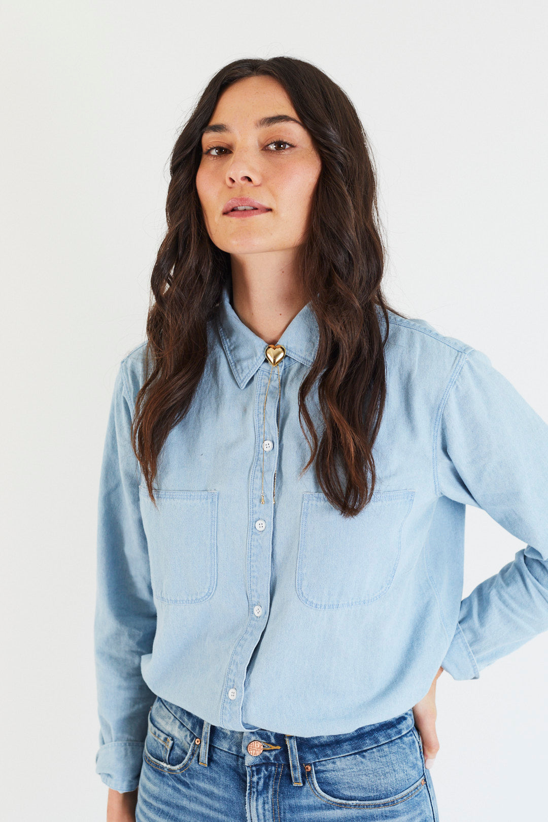 Woman wearing a light blue denim shirt and jeans on a white background