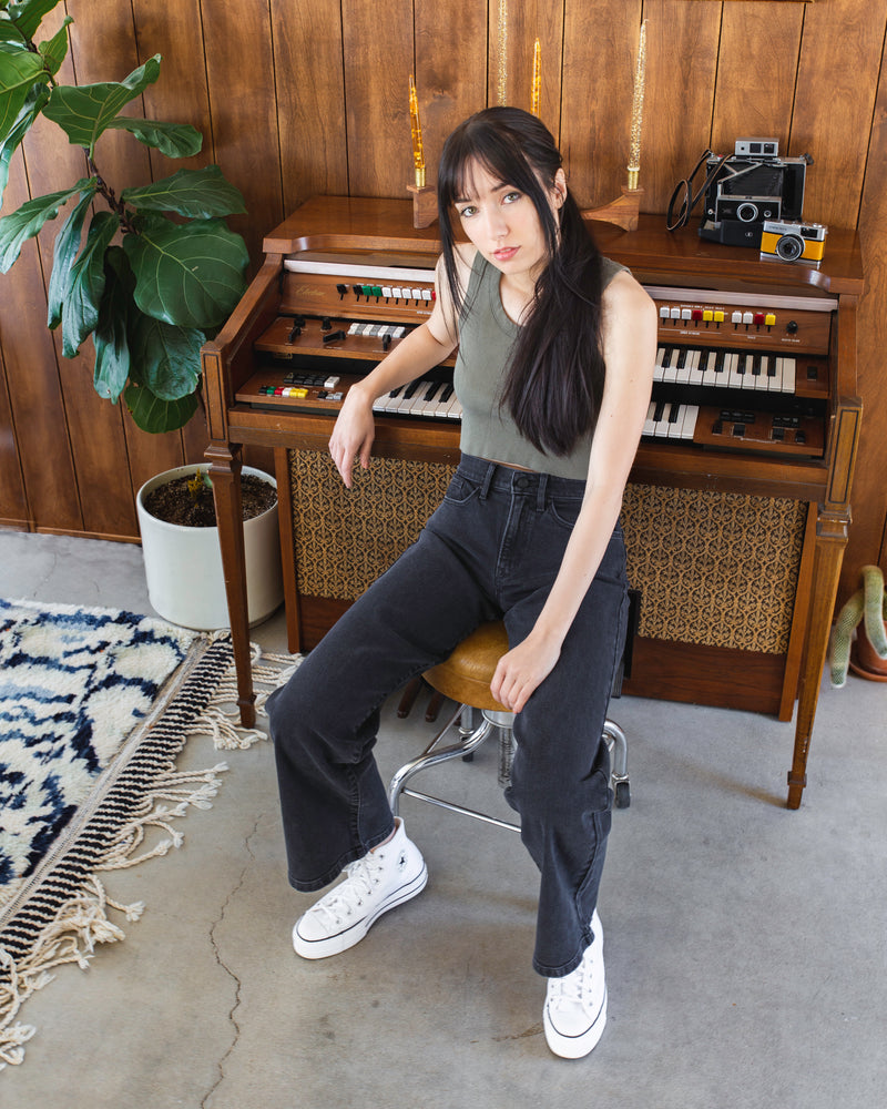 Model sitting in chair at piano wearing Porter Blue Apparel ethically made denim Rebel Wide Leg in Carbon jeans