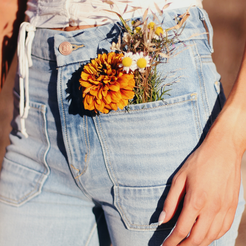 Girl wearing The Wanderer High Rise Flare in Gracie Wash with flowers in front pocket, ethically made jeans by Porter Blue Apparel